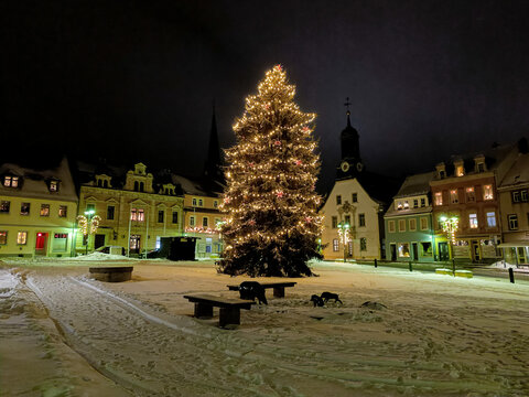winterlicher Marktplatz mit Weihnachtsbaum und Schnee im Lichterschmuck bei Nacht