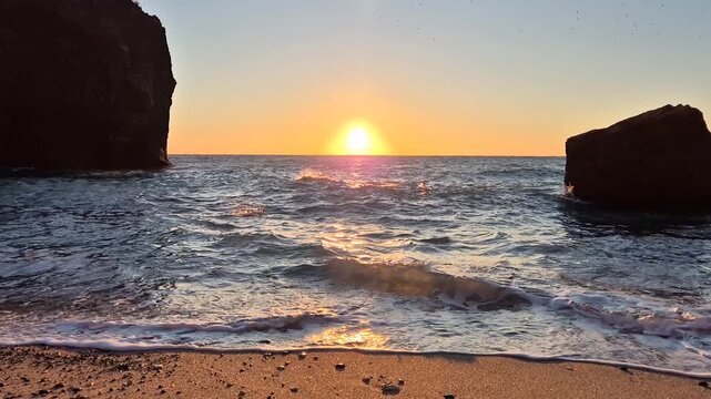 Sunset, ocean, beach golden light reflects on tranquil waves hitting sandy shore between dark rock formations peaceful serene