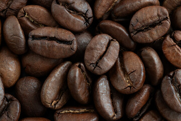 Fototapeta premium A close-up of roasted coffee beans with glossy brown surfaces and visible cracks, conveying warmth and energy. Ideal for coffee branding, recipes, or lifestyle shots.