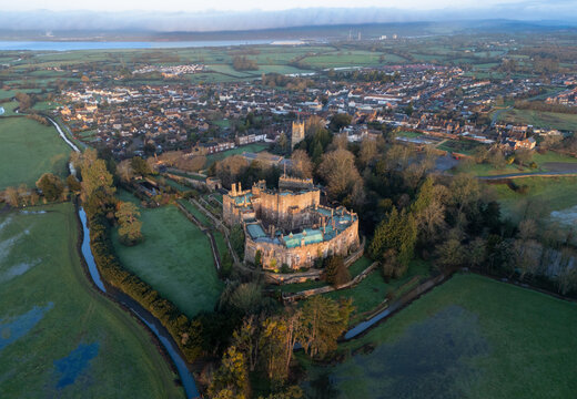 Aerial view of Berkeley Castle stands majestically amidst a sea of green fields, its ancient stones glowing softly in the dawn light, Berkeley, England, United Kingdom.