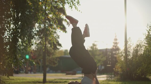 dynamic headstand and flip sunlight, park performance with woman dancer in white top, arms extended into triumphant pose, golden backlight and lens flare, energetic groove and playful mood, outdoor