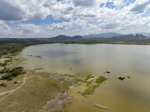 Aerial view of a serene lake reflecting the sky, bordered by lush greenery meeting the water's edge, framed by distant hills, Gilgil, Nakuru, Kenya.