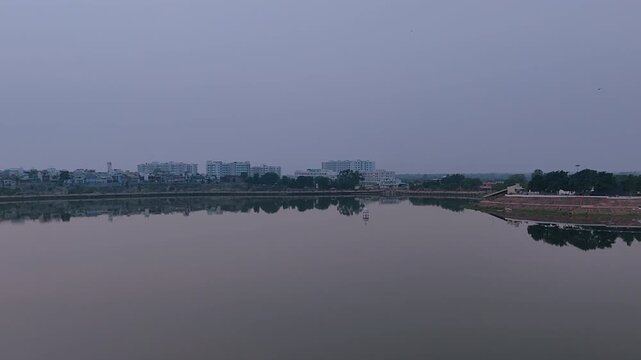 Sharmishtha Lake Vadnagar Gujarat India with calm water reflections, city skyline and evening sky creating peaceful mood for travel, environment, meditation and urban nature themes.