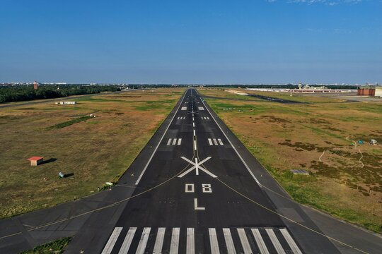 Aerial view of the stark black runway cutting through the golden fields of Flughafen Tegel under a clear blue sky, Berlin, Berlin, Germany.