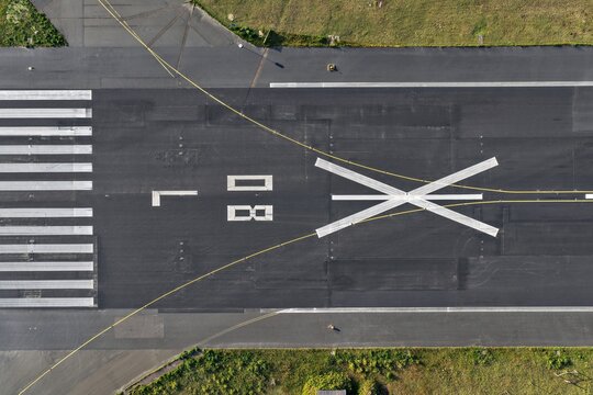 Aerial view of the stark runway markings cutting through the dark asphalt, lined with concrete and bordered by green grass, Flughafen Tegel, Berlin, Berlin, Germany.