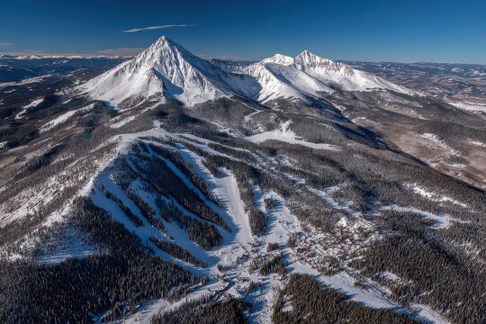 Aerial View of Snow Covered Mountain Range Under a Clear Blue Sky with Dense Evergreen Forests in Winter Landscape - Powered by Adobe