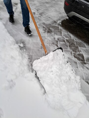 Ein Mann schaufelt Schnee mit einer Schneeschaufel in einer Einfahrt. Winter, K&auml;lte.