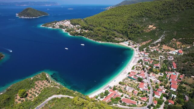 Aerial drone cinematic view of Panormos Bay on Skopelos island, Greece. Scenic coastal road with cars and opens panoramic view of deep blue sea, lush green hills and Dasia islet