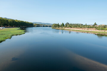 O Contraste entre a tranquila margem do rio Lima, coberta por ervas aqu&aacute;ticas, e a arquitetura da ponte rodovi&aacute;ria ao fundo em Ponte de Lima