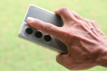 Close-up view with selective focus, a hand holding a modern smartphone with multiple cameras outdoors.
