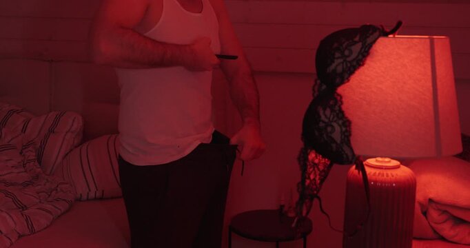 A man uses his smartphone in a red-lit bedroom, implying the sending of an inappropriate explicit image and highlighting digital boundaries, consent, and online harassment.