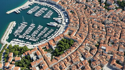 Fototapeta premium Aerial view of a coastal city with a large marina filled with boats and tightly packed red-roofed buildings