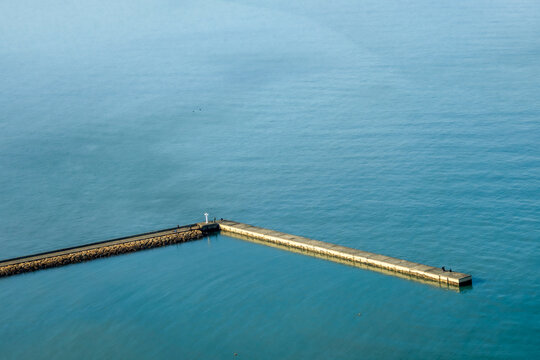 Aerial view of the stark, linear pier stretching into the tranquil sea, contrasting textures and hues, Momochihama, Sawara Ward, Fukuoka City, Japan.