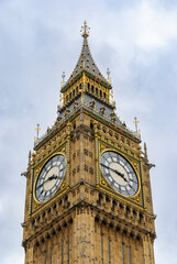 Low-angle view of Big Ben (Elizabeth Tower) in London, showcasing ornate Gothic details and golden clock faces against a pale sky.