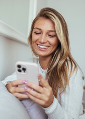 Happy Woman Smiling At Smartphone While Relaxing At Home In Cozy White Sweater