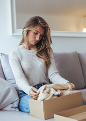 A Cozy Woman Unpacking a Cardboard Box with Knit Sweater on Sofa at Home Today