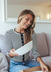 Happy Woman Opens Package At Home, Enjoying Plate While Smiling On Living Room Couch