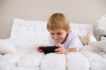 blonde little boy using smartphone lying on the bed