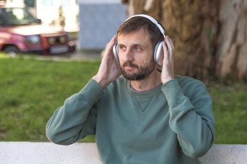 Man wearing wireless headphones while relaxing outdoors, listening to music in urban park, calm moment, modern lifestyle, audio technology, mindfulness concept, real people