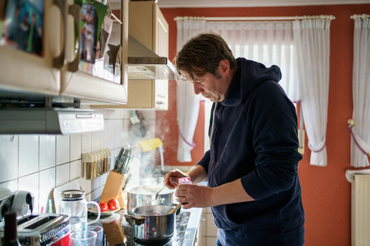 Man cooking meal for family lunch with pasta and meat in domestic kitchen and serving table