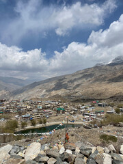 Obraz premium View of a mountain village surrounded by clouds and hills in the daytime with a river running through it