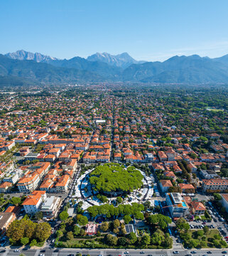 Aerial view of the vibrant green roundabout contrasting against the terra-cotta rooftops, with the majestic Apuan Alps looming in the distance, Forte dei Marmi, Tuscany, Italy.