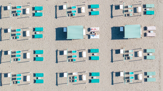 Aerial view of organized beach umbrellas and sunbeds cast long shadows on the sand, creating a geometric pattern of light and shade, Forte dei Marmi, Tuscany, Italy.