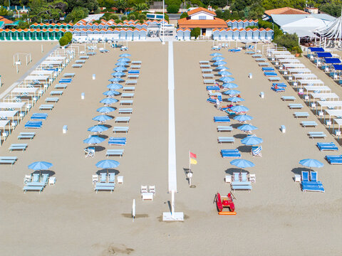 Aerial view of symmetrical rows of sunbeds and umbrellas on the sandy beach, framed by orderly beach huts, casting shadows under a bright sky, Forte dei Marmi, Tuscany, Italy.