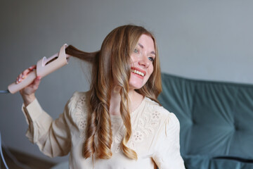 Lifestyle beauty image of smiling woman using hair styling tool in minimal cozy interior