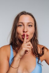 Fototapeta premium Woman with long hair in blue top placing finger on lips in indoor setting during daytime