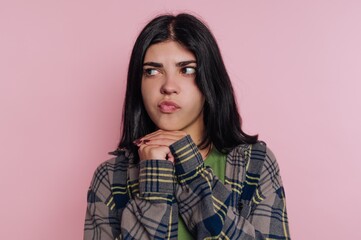 Fototapeta premium Girl with dark hair wearing a checkered jacket is looking thoughtfully against a pink background