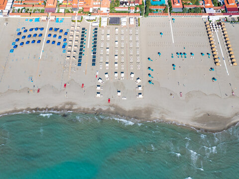 Aerial view of neat rows of sunbeds and umbrellas dotting the sandy beach meeting the turquoise sea, Forte dei Marmi, Tuscany, Italy.