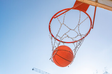 Basketball Ball Falling into the Hoop with Metal Chain Net on Outdoor Court © Iliya Mitsk