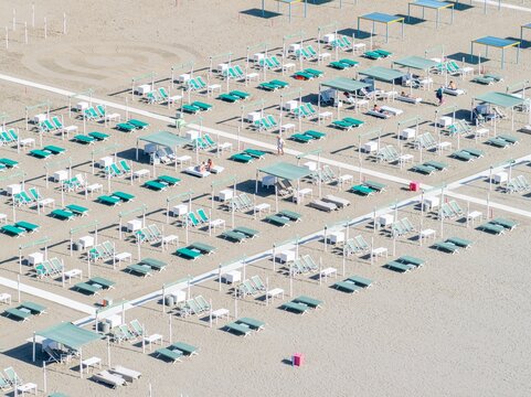 Aerial view of neatly arranged beach umbrellas and sunbeds casting shadows on the sandy shore, creating a symmetrical pattern of relaxation, Forte dei Marmi, Tuscany, Italy.