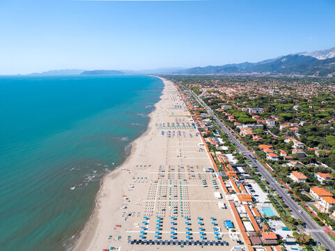 Aerial view of the striking contrast between the turquoise sea and the golden beach lined with neat rows of sun umbrellas, backed by a vibrant town, Forte dei Marmi, Tuscany, Italy.