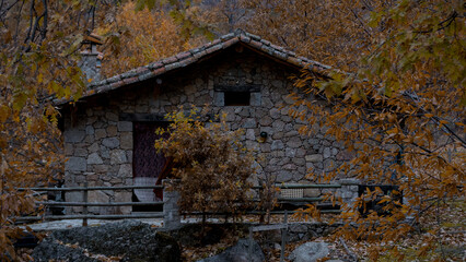 Cabaña rústica de piedra rodeada de árboles con follaje naranja intenso en otoño.
