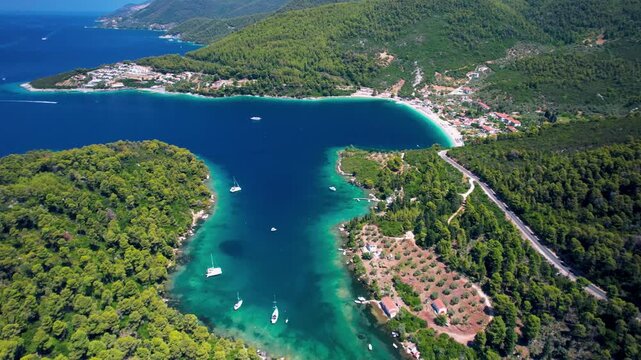 Stunning drone aerial view of Panormos Bay and Blo harbor on Skopelos island, Greece. Turquoise sea water with anchored yachts and lush green hills 