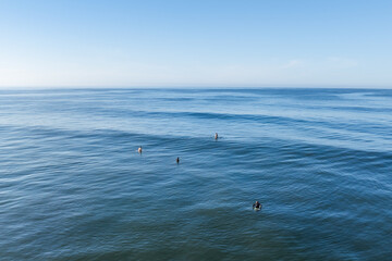 Aerial view of surfers dotting the vast expanse of the deep blue sea under a clear sky, creating a serene yet dynamic seascape, La Saladita, Guerrero, Mexico.