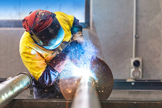 worker welding metal. A skilled industrial worker carefully welding a large metal pipe inside a modern workshop, wearing full protective gear as bright sparks and intense light capture the precision