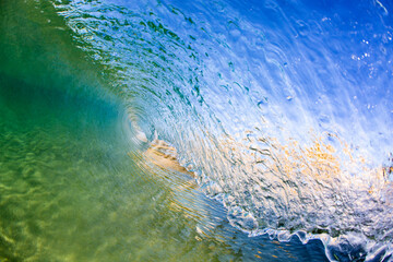 A beautifully textured crystal clear ocean wave curling and breaking over a shallow shoreline. Captured from within the wave on an Illawarra South Coast beach on a bright sunny day.