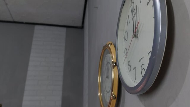 Footage of an analog quartz wall clock made in Japan, hanging on a gray painted wall.