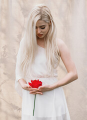 A blonde girl with long hair holding a red flower. Her downcast gaze signifies intimacy, a symbol of the menstrual cycle and PMS. Femininity is a figurative embodiment of gynecology.