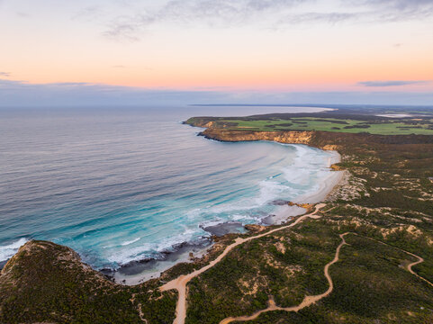 Aerial view of the rugged coastline meeting the turquoise waters, contrasting with the green vegetation and sandy beach, Port Willunga, South Australia, Australia.