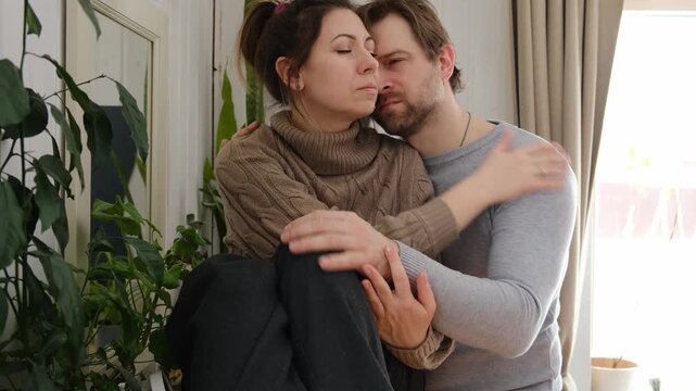 Couple comforting embrace together. Man holds woman with gentle embrace wearing casual clothes, muted living room background. Soft natural light. Tender emotional connection as they provide quiet