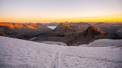 The sun rises over Pers Glacier, illuminating the Bernina Range's rugged peaks. The serene landscape showcases the breathtaking beauty of the Swiss Alps at dawn.