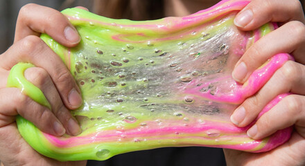 Close up of hands stretching neon green and pink translucent slime representing sensory play and fun, visual asmr