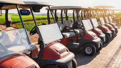 Luxury golf carts parked on a path near the green fields at a golf course during sunset