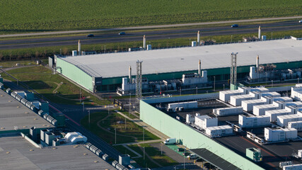 Aerial view of the vast, low-slung data center complex with its muted green and grey hues against the backdrop of the highway, AI Data Center, Middenmeer, Netherlands.