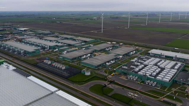 Aerial view of rows of industrial green buildings and containers under a cloudy sky, Agriport, Middenmeer, Netherlands.