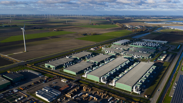 Aerial view of a sprawling data center complex juxtaposed against the flat landscape, windmills standing tall in the distance, Middenmeer, Netherlands.